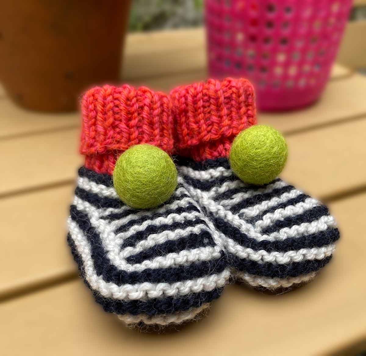 Hand Knitted baby booties with red tops and striped pattern on a wooden surface - made by Lilly and Bright