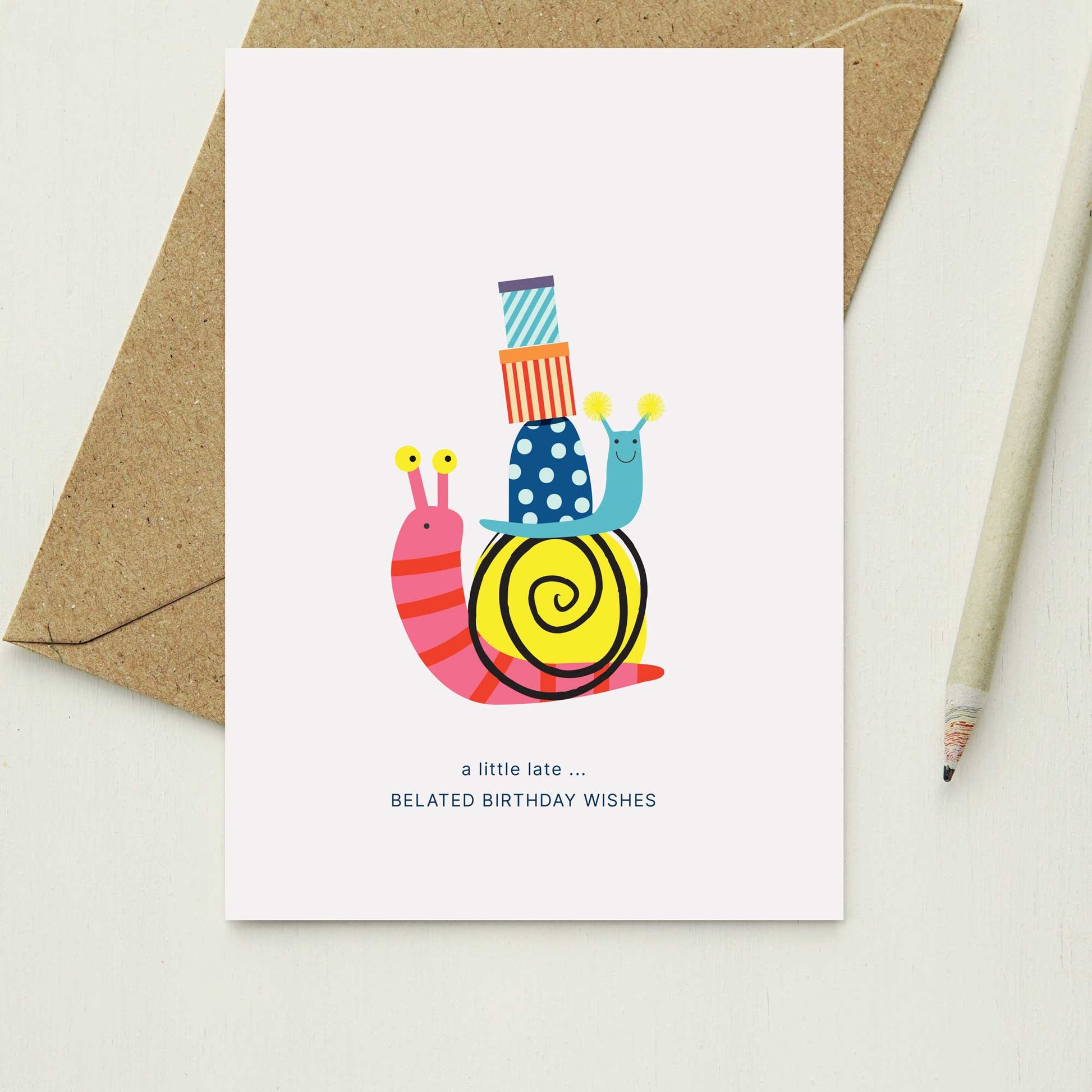 A6 belated Birthday card with two snails carrying birthday gifts.On a white background with a kraft envelope and pencil.