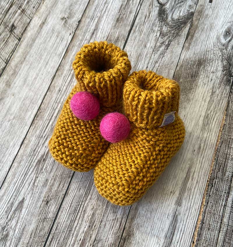 Handknitted Mustard Baby Booties with a pink felt pompom by Lilly & Bright