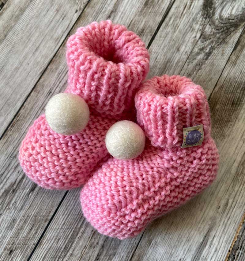 pink handknit baby booties with a cream pom pom by lilly and bright