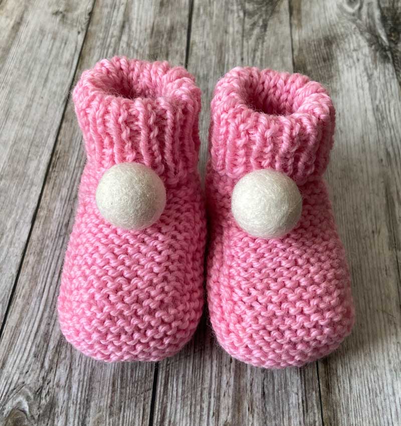 pink handknit baby booties with a cream felt pom pom by lilly and bright